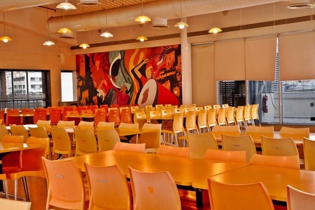 Fifth floor cafeteria with long communal tables and windows on three sides.